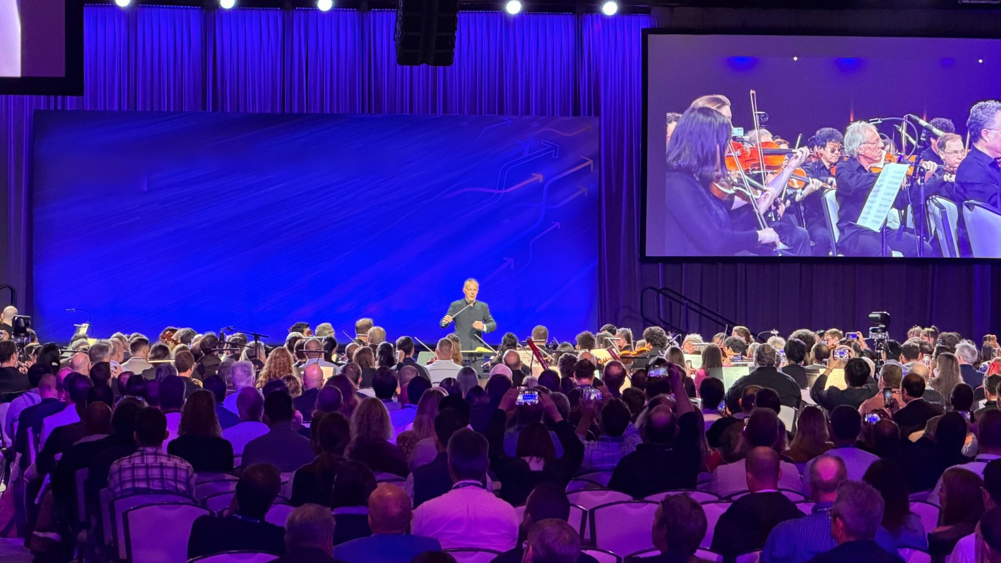Conductor leading a live orchestra for a packed ballroom audience during an executive event